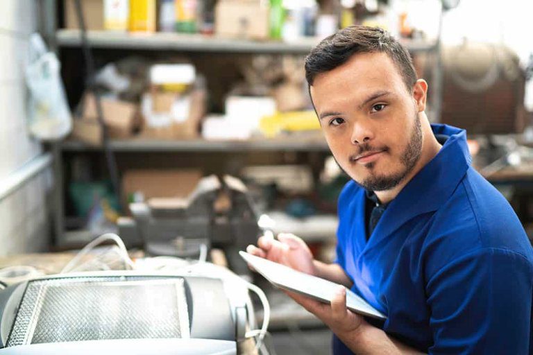 Mann in Arbeitsklamotten in einer Werkstatt mit einem Tablet in der Hand